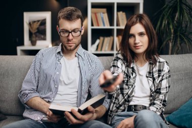 Erkeği kitap okurken kadın televizyon seyrediyor.