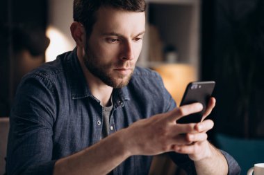 Genç adam evde akıllı telefon kullanıyor.