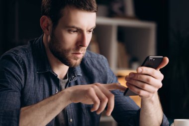 Genç adam evde dinleniyor ve cep telefonu kullanıyor.