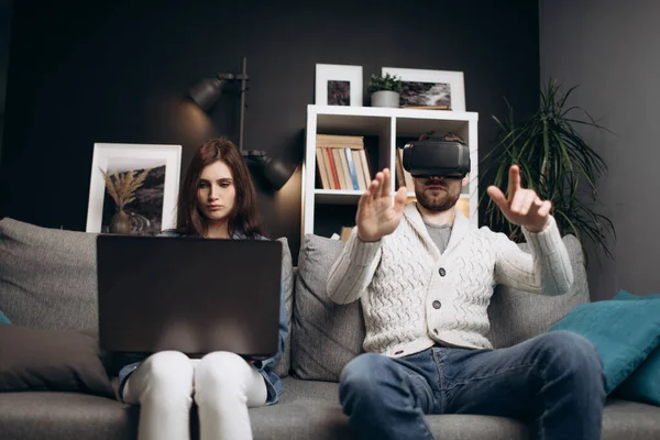 Giovane coppia utilizzando laptop e VR auricolare a casa — Foto Stock