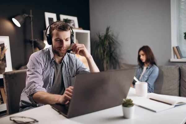 Muž má video chat na notebooku, zatímco žena čte knihu — Stock fotografie