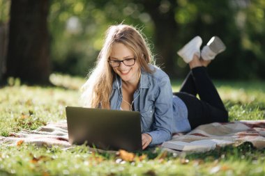 Parkta dizüstü bilgisayarda çalışırken mutlu bir sarışın.