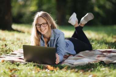 Parkta yatan ve dizüstü bilgisayarla internette sörf yapan kadın.
