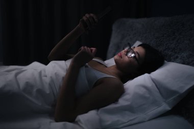 Yatakta akıllı telefonlu bir kadın