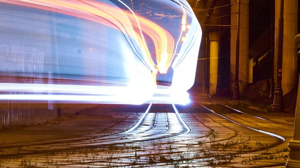 Şehirde toplu taşıma. İstasyondan ayrılan tramvay, trafik ışıkları, insanlar, sokak, evler, teller, raylar. Hareket ve ışıklar, uzun pozlama.