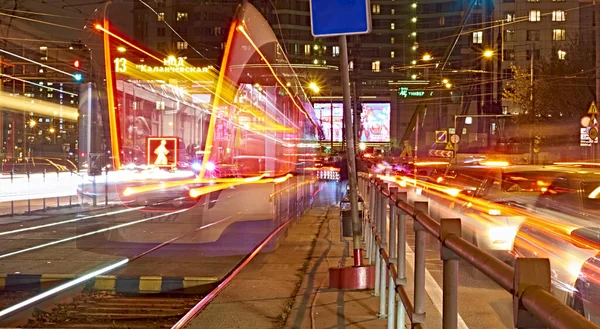 Public transportation in a city. Tram leaving the station, traffic lights, people, street, houses, overhead wires, rails. Movement and lights, long exposure.