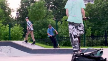 Rusya Moskova 2020. Çocuklar, gençler sonbaharda ekstrem spor sokak paten parkında kaykay ve scooter kullanıyor. yavaş çekim