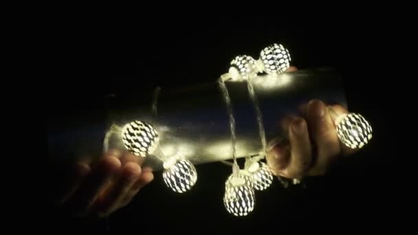 Muzikale instrument shaker in de handen van een vrouw verkleed met een kerstslinger. Nieuwjaarsstemming. bij weinig licht. close-up. kleur — Stockvideo