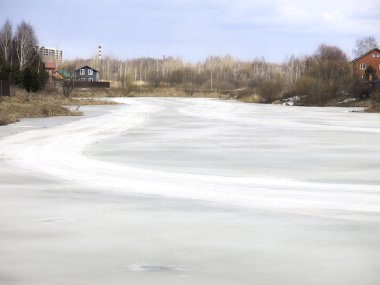 Köy göleti, uzak mesafede sıcak evleri olan bahar buzu kabuğuyla kaplı.
