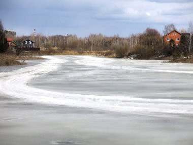 Köy göleti, uzak mesafede sıcak evleri olan bahar buzu kabuğuyla kaplı.