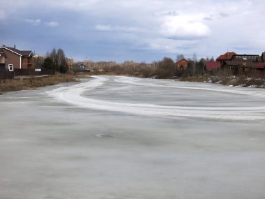 Köy göleti, uzak mesafede sıcak evleri olan bahar buzu kabuğuyla kaplı.