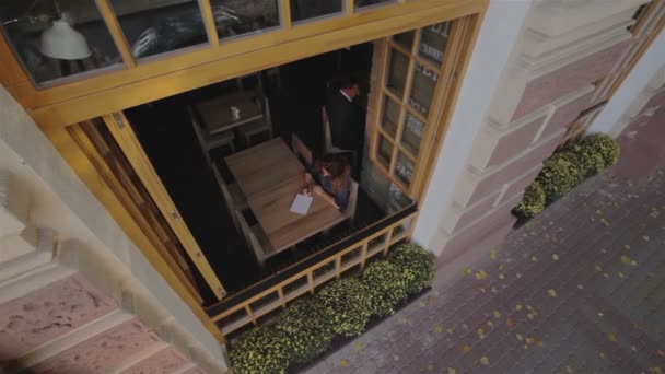 CRANE MOTION: La chica en el café escribió en su cuaderno. Vista desde la altura de la calle . — Vídeos de Stock