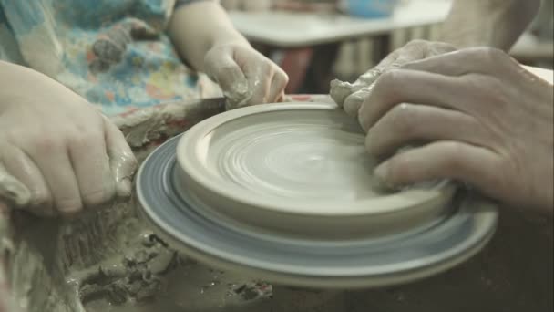 Las manos de un alfarero le muestran al niño cómo trabajar para ayudarlo a trabajar con la rueda de cerámica. Grabación de vídeo RAW . — Vídeos de Stock