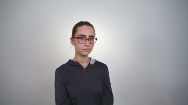 Gleichgültiger Blick eines Mädchens mit Brille vor weißem Hintergrund. Rohe Videoaufzeichnung. — Stockvideo