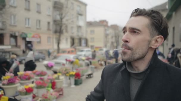 Un hombre guapo con barba en un impermeable en la calle fumando — Vídeos de Stock