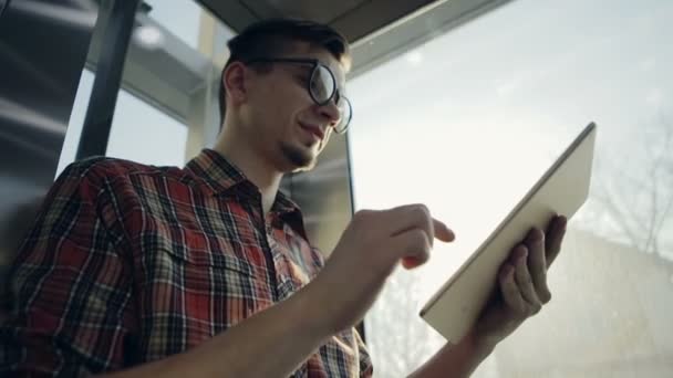 En ung man lyfta upp av hissen blir lycklig med sin elektroniska enhet — Stockvideo