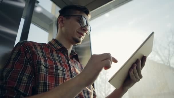 Un joven levantándose junto al ascensor se está volviendo feliz con su dispositivo electrónico — Vídeo de stock