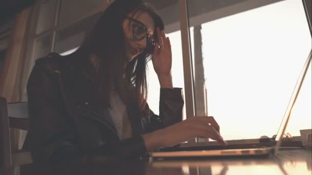 Mooie vrouw met laptop zitten aan een tafel in de ochtendzon en te typen. Ruwe videoverslag. — Stockvideo