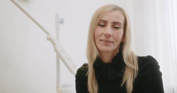 Senior kvinna med vitt hår med rynkor i ansiktet tittar på kameran och ler sitter i en skönhetssalong orolig före ingreppet — Stockvideo