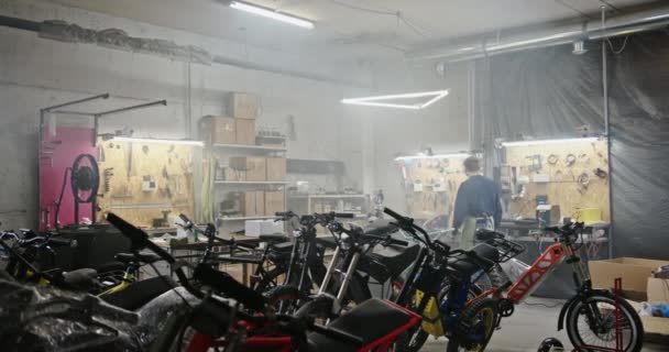 Тернополь, Украина, 21 января 2021 года: Мужской механик идет к стенду в гараже. Увеличите масштаб с учетом анонимной техники, идущей к рабочей скамейке и начинающей работать рядом с пользовательскими мотоциклами — стоковое видео