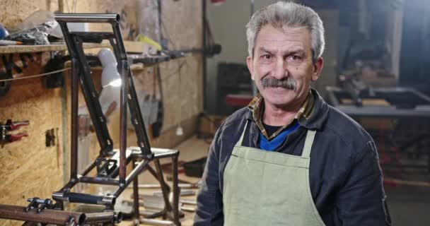 Pozytywny starszy technik w warsztacie. Pewny siebie starszy mechanik przecinający ramiona i patrzący z uśmiechem na kamerę podczas pracy w garażu — Wideo stockowe
