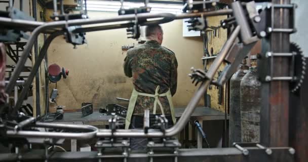 Un giovane uomo lavora sul posto di lavoro dove salda parti metalliche a biciclette elettriche nella sua officina sparando dal retro senza una faccia — Video Stock