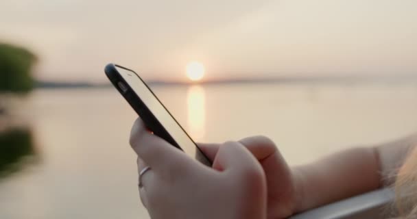 Close-up de smartphone em mãos meninas ganha mensagem de texto na rede social em meio ao pôr do sol quente no verão — Vídeo de Stock