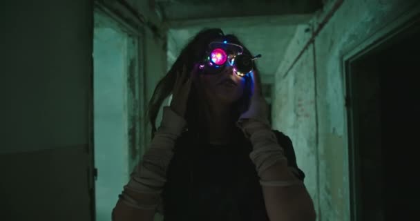 Девушка-робот из будущего с искусственным интеллектом и цветными светящимися очками бродит по заброшенному зданию и видит, как странные вещи улыбаются самой себе. — стоковое видео