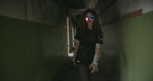 En futuristisk flicka med mänsklighetens apokalyps i underliga fantastiska glasögon djärvt när en robot går ner i korridoren i en krigshärjad byggnad. — Stockvideo