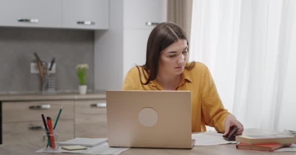 Excited female student receiving good news. Young woman with laptop reading message on smartphone then screaming in excitement while studying in kitchen at home — Stock Video