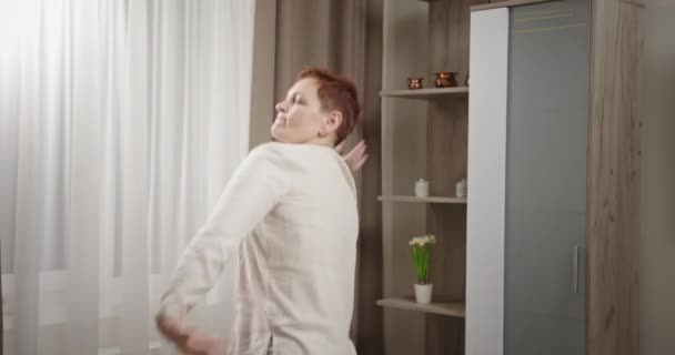 Kvinnan dansar aktivt och hoppar av glädje och viftar med armarna leende hemma i vardagsrummet. Galet kul dans efter jobbet — Stockvideo