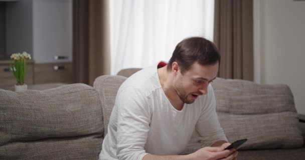 L'uomo si rallegra di vincere su smartphone emozioni positive buone notizie seduti a casa sul divano a casa luce nuovo cratere — Video Stock