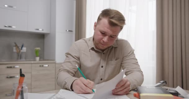 Człowiek zapisujący słowa klienta. mężczyzna freelancer kiwanie głową i pisanie na papierze siedząc przy stole w kuchni i słuchając klienta — Wideo stockowe