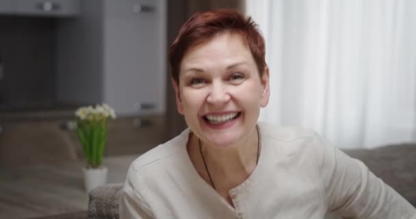 Conversación en línea conferencia emocional. Mujer hablando en video saludando sonriendo sorprendida por las noticias sentada en casa en el sofá — Vídeos de Stock