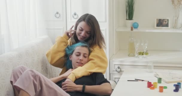 Dos jóvenes amantes lesbianas compartiendo un momento feliz y tierno juntos mientras se abrazan en un sofá en casa riendo y sonriendo — Vídeos de Stock