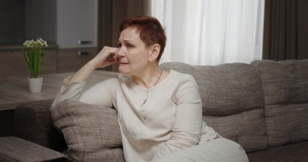 Депресивна апатична жінка, що сидить на дивані вдома стурбована плачем закриває обличчя руками, відчуває поганий настрій від негативних емоцій — стокове відео