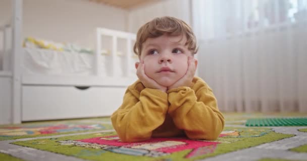 Leuke jongen die op de vloer rust. Begane grond van schattige jongen liggend in tapijt en ontspannen in gezellige kinderkamer in het weekend thuis — Stockvideo
