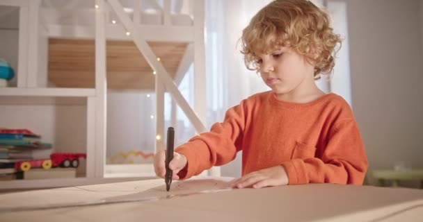 Malý bílý kudrnatý chlapec kreslí s fixem zaměřený se snaží rozvíjet kreativitu ve svých útulných světlých dětských pokojových snů — Stock video