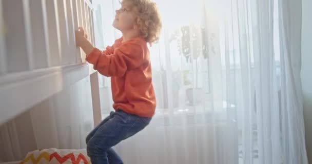 Ternopil, Ukraine, October 6, 2020: Boy climbing on bed at home. Tracking shot of boy with curly hair climbing on bunk bed in light nursery at home — Stock Video