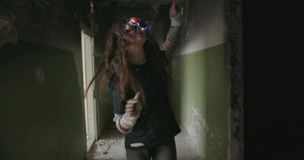 Ein Mädchen aus der Zukunft der neueste Roboter von einem anderen Planeten mit farbigen Brillen geht auf einem verlassenen Gebäude nach der Apokalypse Tänze lächelt zeichnet mit ihren Händen sieht verschiedene Dinge — Stockvideo