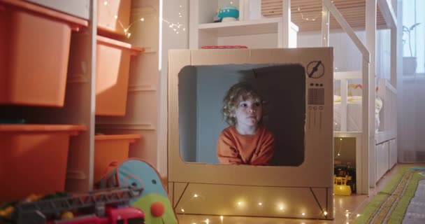 Веселый мальчик сидит в картонном телевизоре и разговаривает — стоковое видео