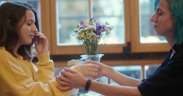 Young lesbian woman giving her partner a gift on a special occasion in a close up view at a restaurant table with flowers in a concept of LGBT relationships — Stock Video