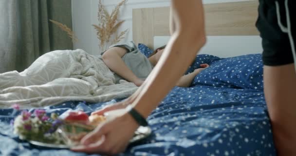 Due giovani ragazze lesbiche sdraiate a letto in un'accogliente camera da letto luminosa che fanno colazione sorridendo. Colazione a sorpresa a letto per la sua amata ragazza con i capelli blu — Video Stock