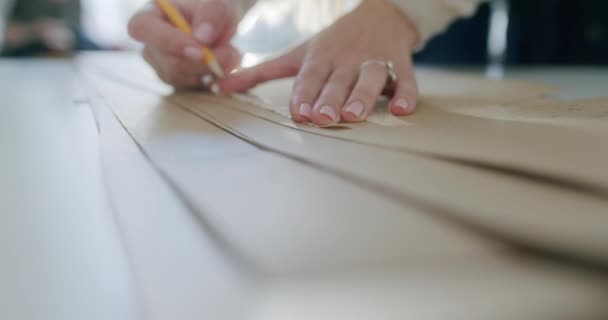 Werkplaats in ontwerpstudio. Jonge vrouwelijke ontwerper tekent platte papieren patronen met behulp van meetlint en rondingen op wazige achtergrond van tailor atelier interieur. Exclusieve kleding maken concept. — Stockvideo