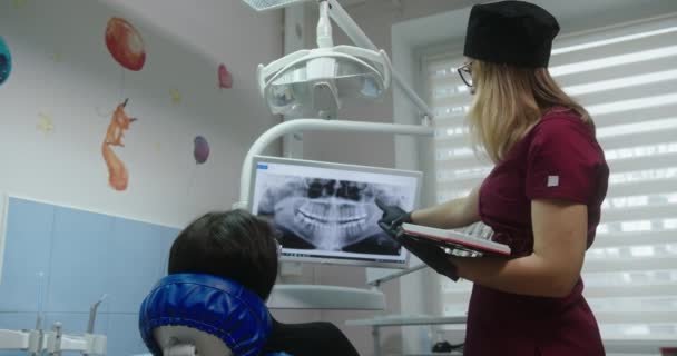 Kobieta lekarz ortodonta pokazuje zdjęcie rentgenowskie pacjenta opowiada o problemie i procesie leczenia w fotelu stomatologicznym szpitala stomatologicznego — Wideo stockowe