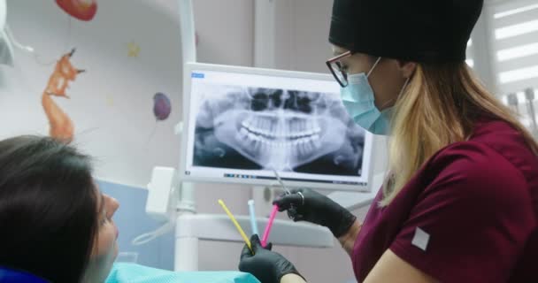 Der Zahnarzt zeigt der Patientin eine Ligatur eines Gummibands für Zahnspangen, so dass sie sich aussucht, wer im Krankenhaus auf dem Zahnarztstuhl sitzen will — Stockvideo