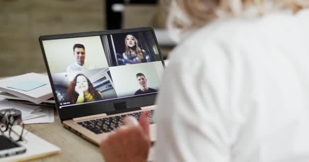 Egy nő vállnézete felett egy videohíváson, ahol a családja látható a laptopja képernyőjén a távoli kommunikáció koncepciójában a koronavírus vagy a Covid-19 járvány idején. — Stock videók