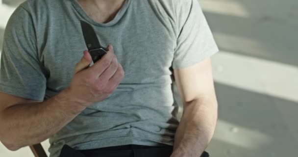 Joven loco con un cuchillo en las manos sentado en una habitación abandonada se corta el pelo se siente deprimido y apatía deprimida — Vídeos de Stock