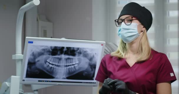 Женщина-дантист, стоящая рядом с монитором с рентгеном зубов — стоковое видео