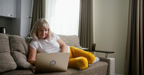Kanepede dizüstü bilgisayar kullanan yaşlı kadın. — Stok video